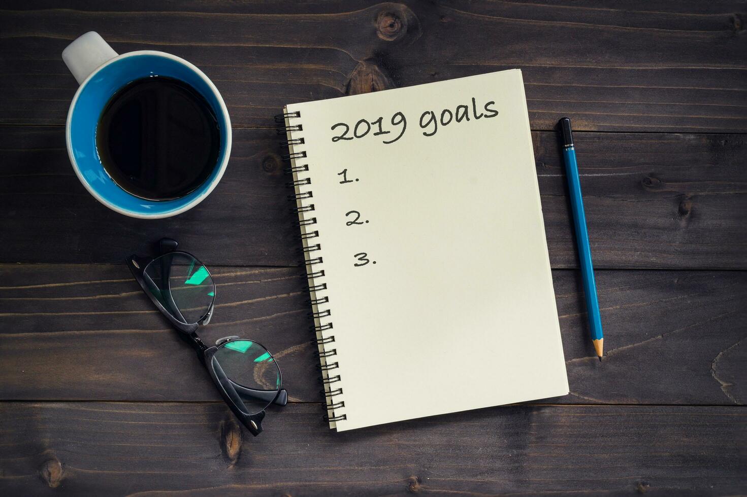 Notebook with 2019 goals massage, pencil, glasses and cup of coffee on wood background. photo