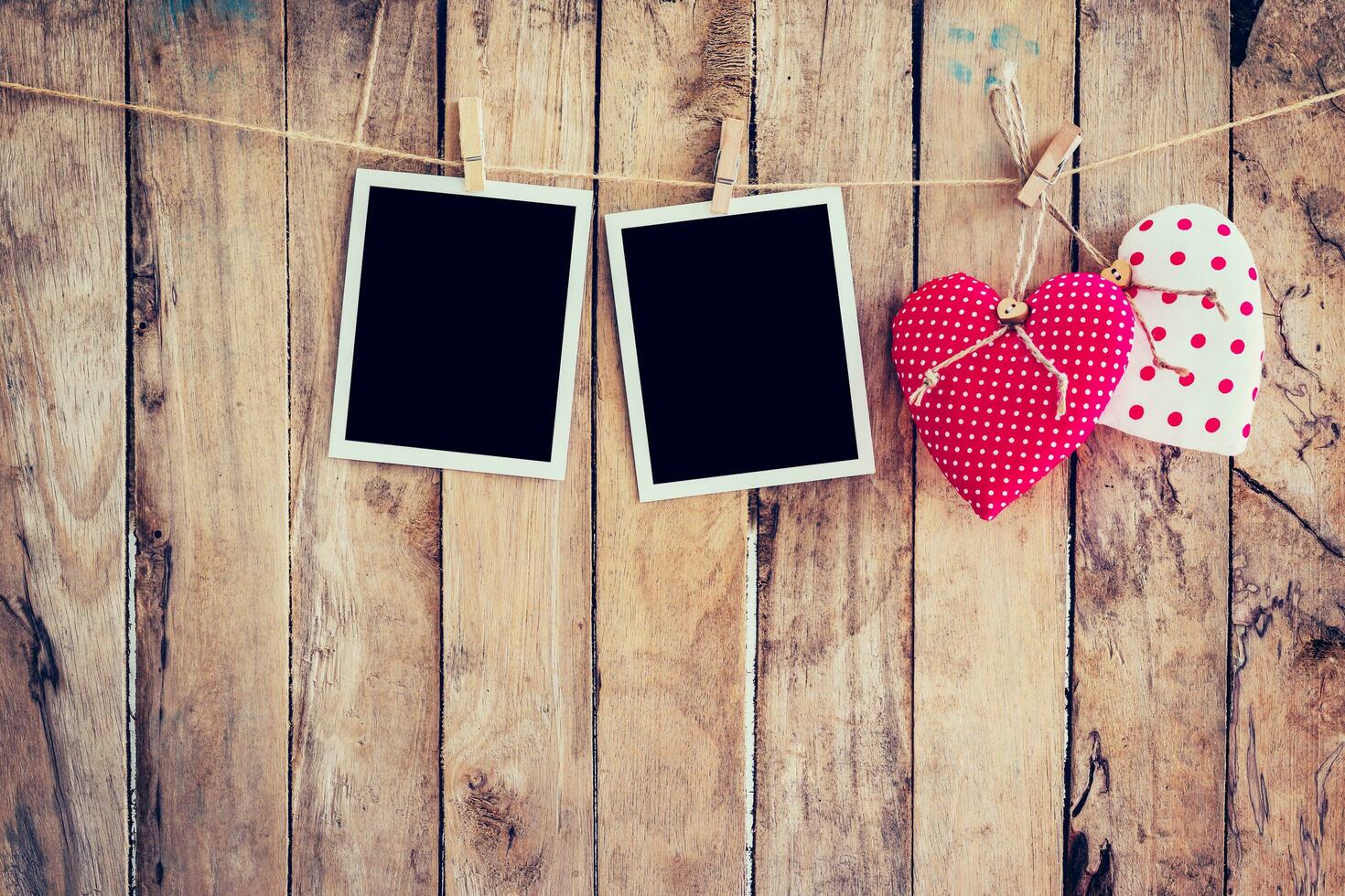 Red heart and two photo frame hanging on clothesline rope with wooden background.