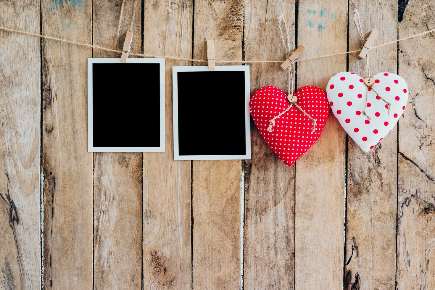 Two heart and two photo frame hanging on clothesline rope with wooden background.