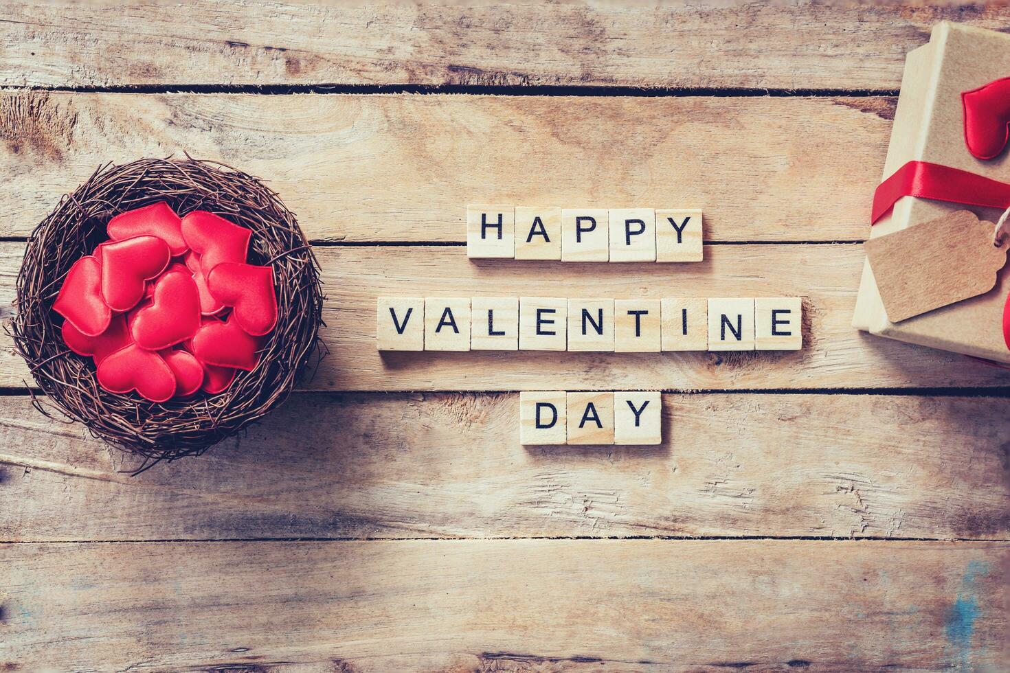 Gift box and red heart in nest with wooden text Happy Valentine Day on wood table background. photo