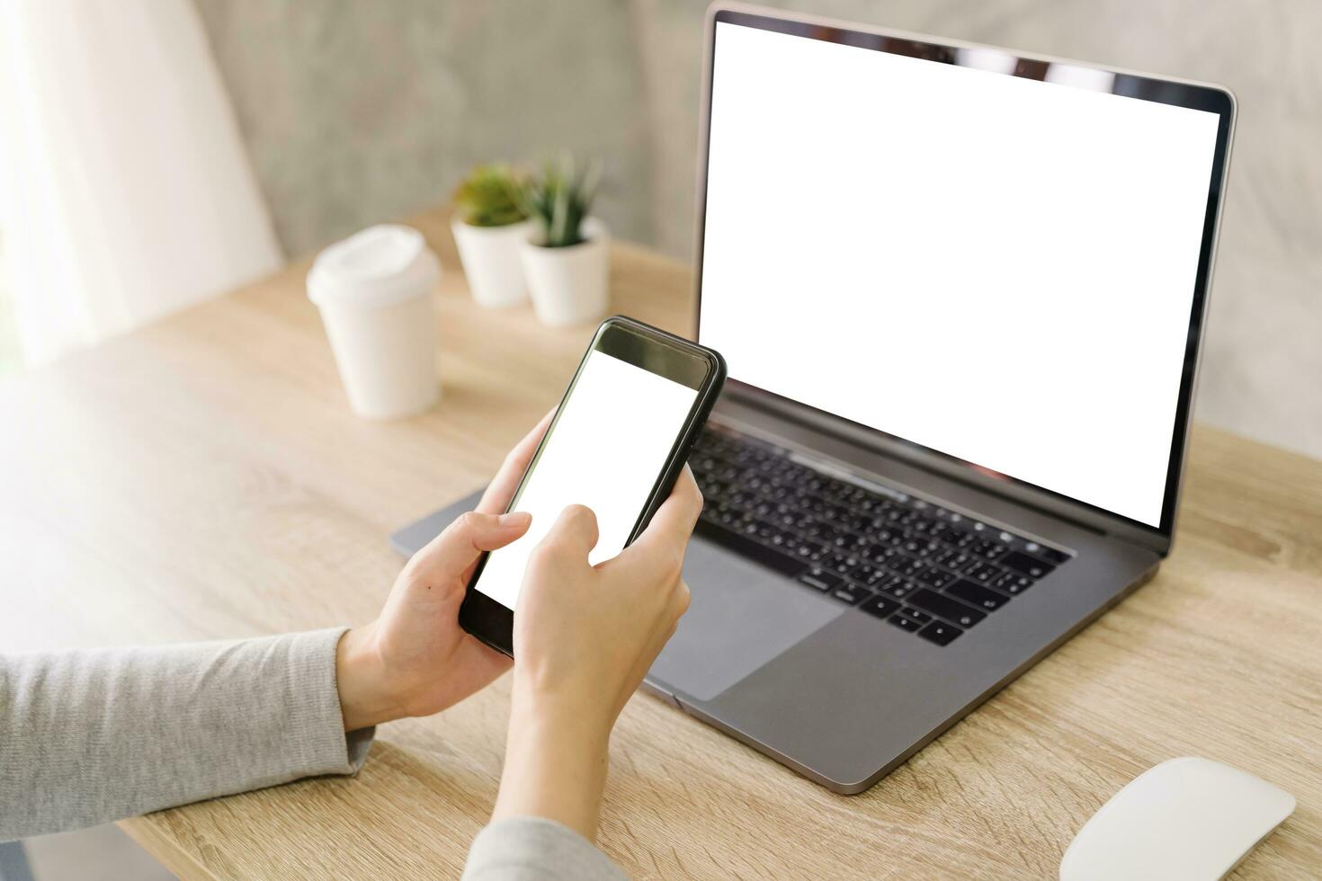 Asian woman holding phone and using computer laptop on wooden table photo