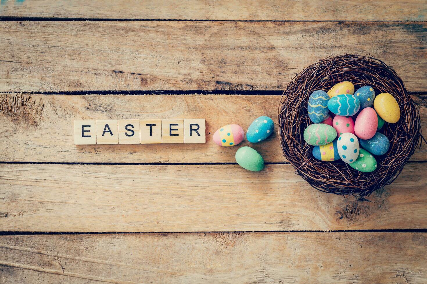 Colorful easter egg in the nest and wood text for Easter on wood background with space photo