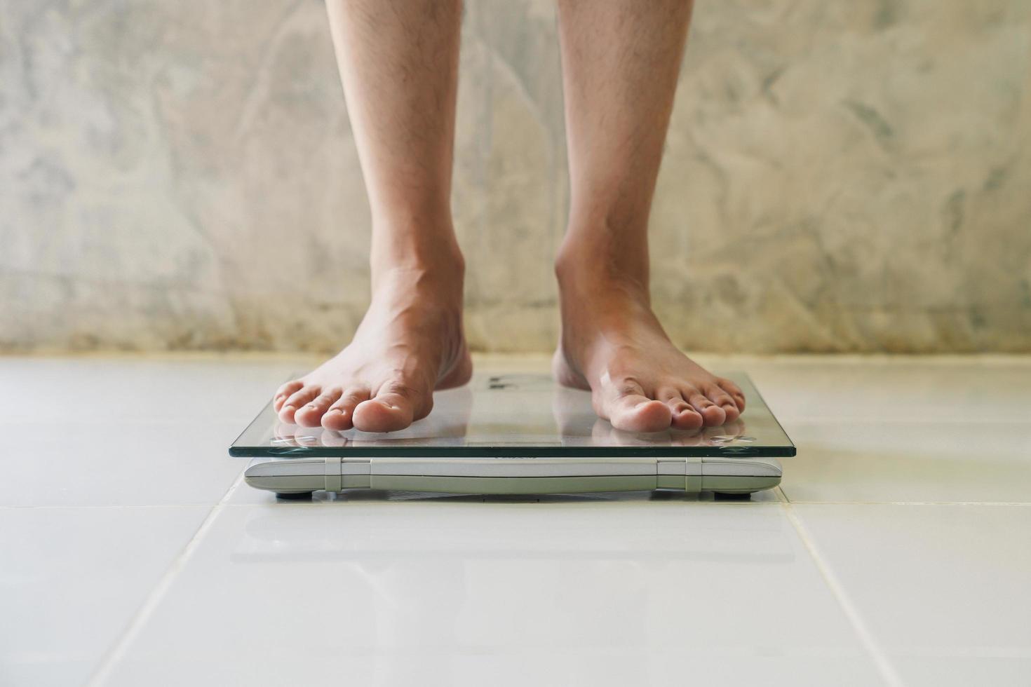 masculino en peso escala en piso fondo, dieta concepto. foto