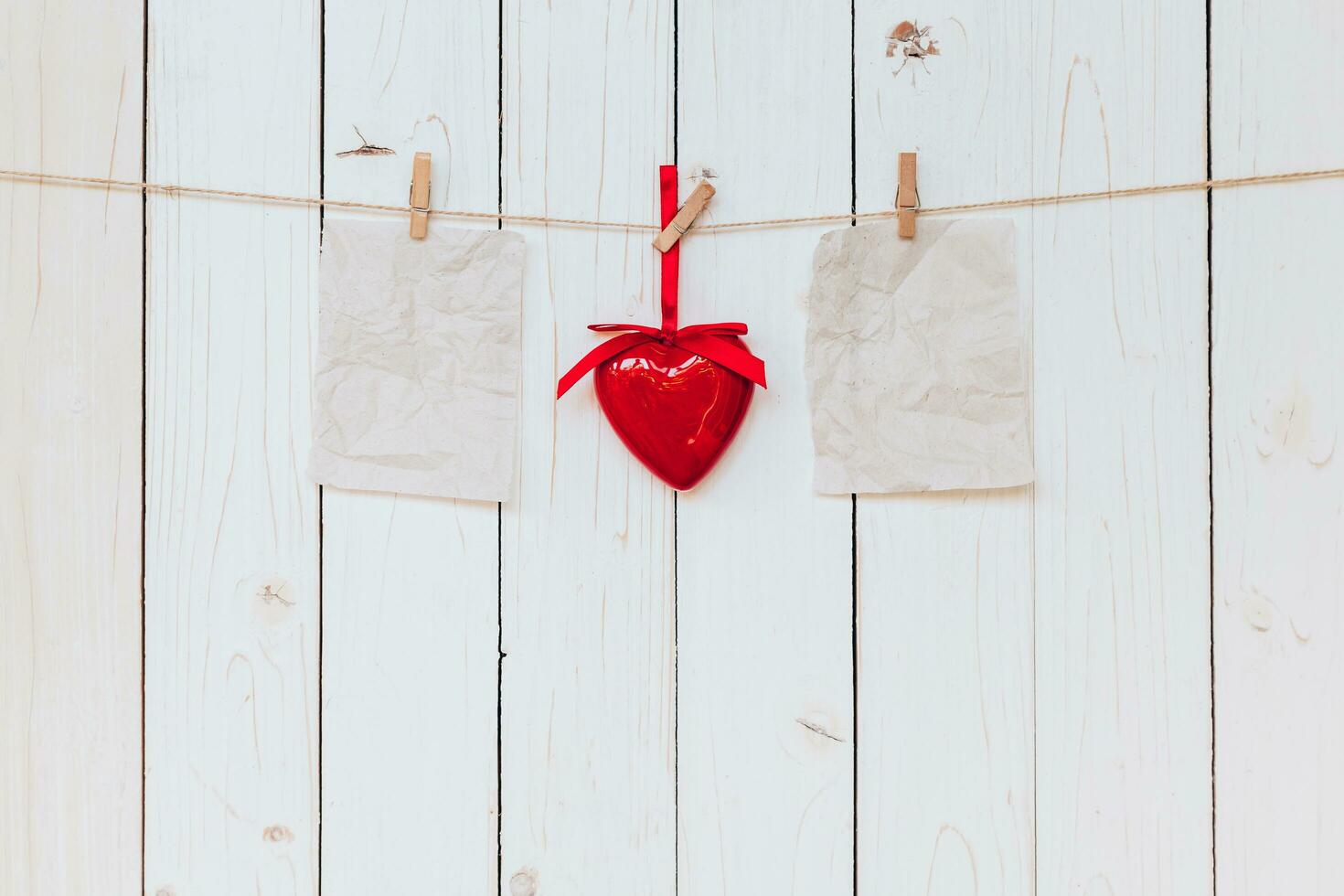 Red heart and old paper blank hanging at clothesline on wood white background with space. Valentine Day. photo