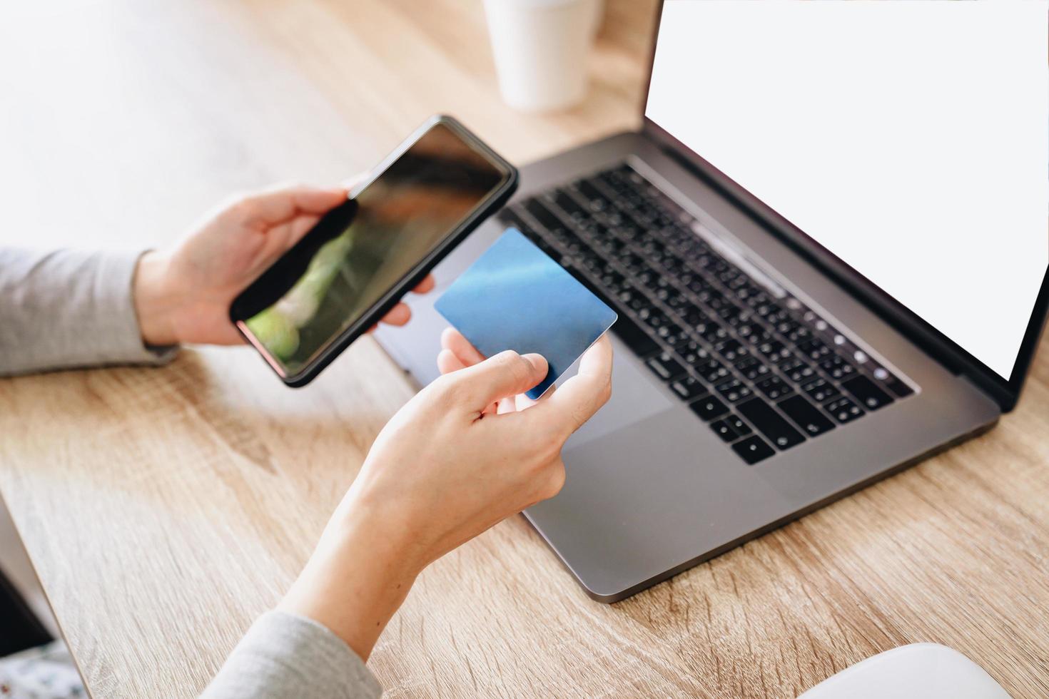 Asian woman holding credit card paying for shopping on mobile phone with computer laptop on wooden table photo