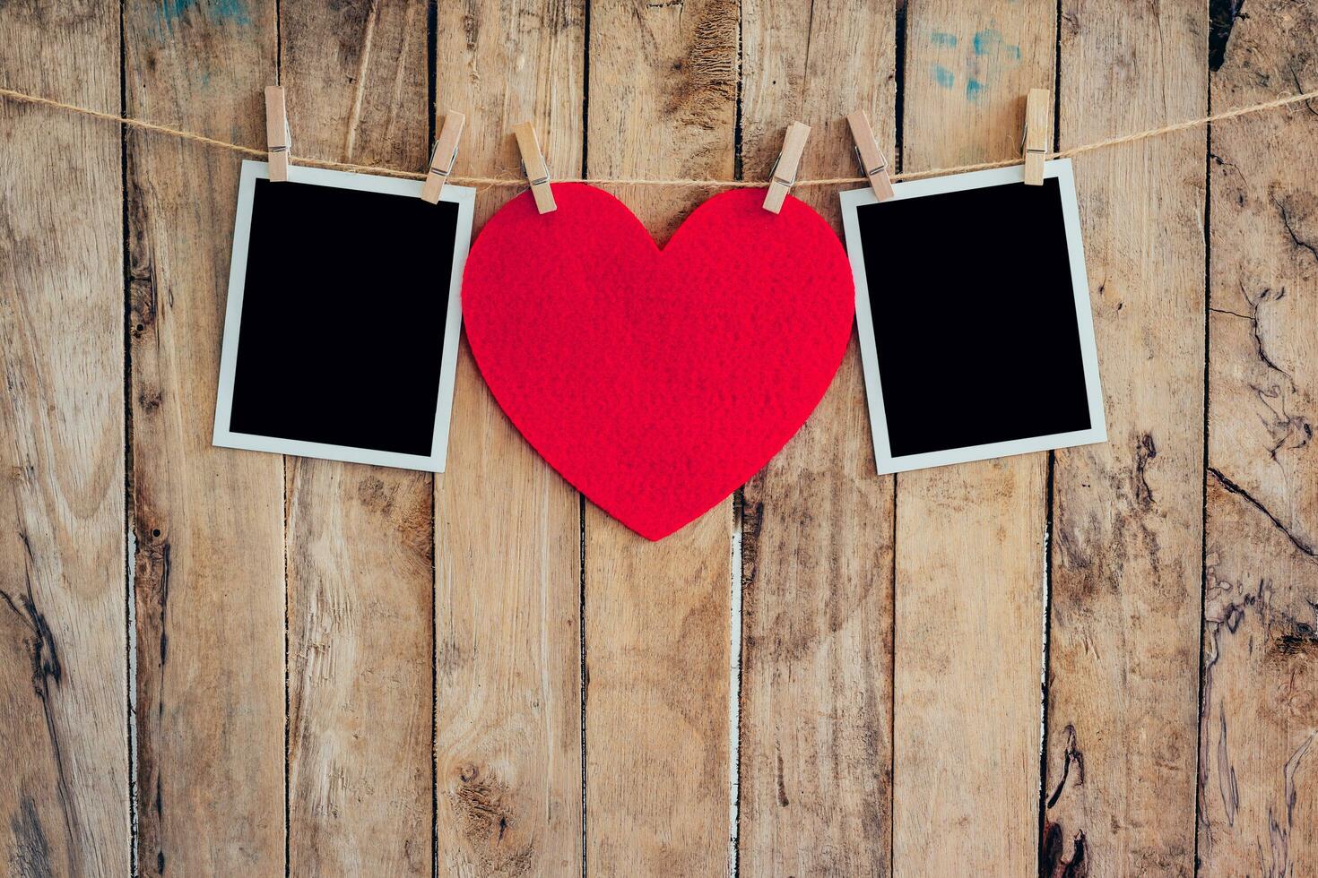 Red heart and two photo frame hanging on clothesline rope with wooden background.