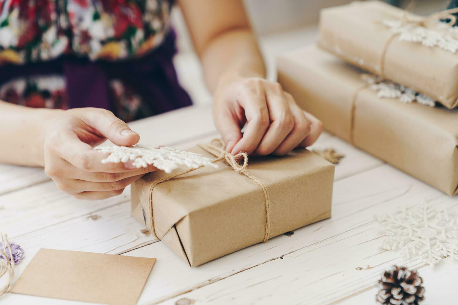 Close up of hands holding wrapping gift box on wooden table with xmas decoration. photo