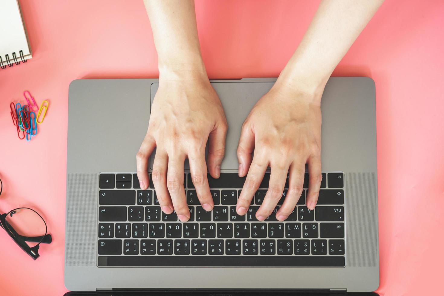 Women typing on laptop in pink pastel colourful office with accessories photo
