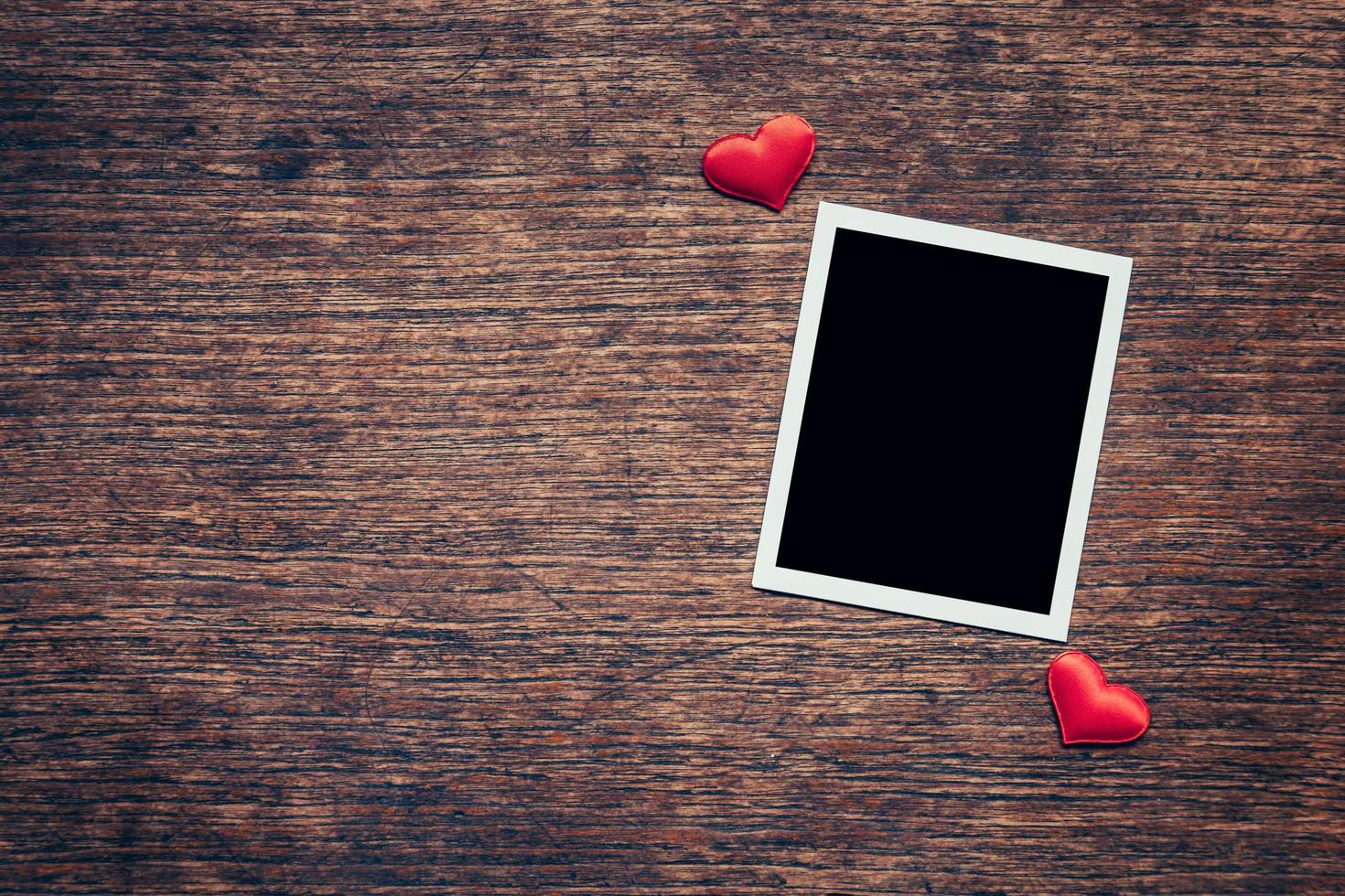 Blank photo frame and red heart on wood background with space.