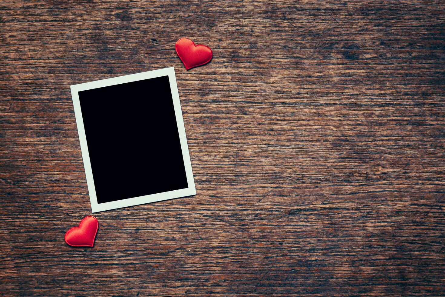 Blank photo frame and red heart on wood background with space.