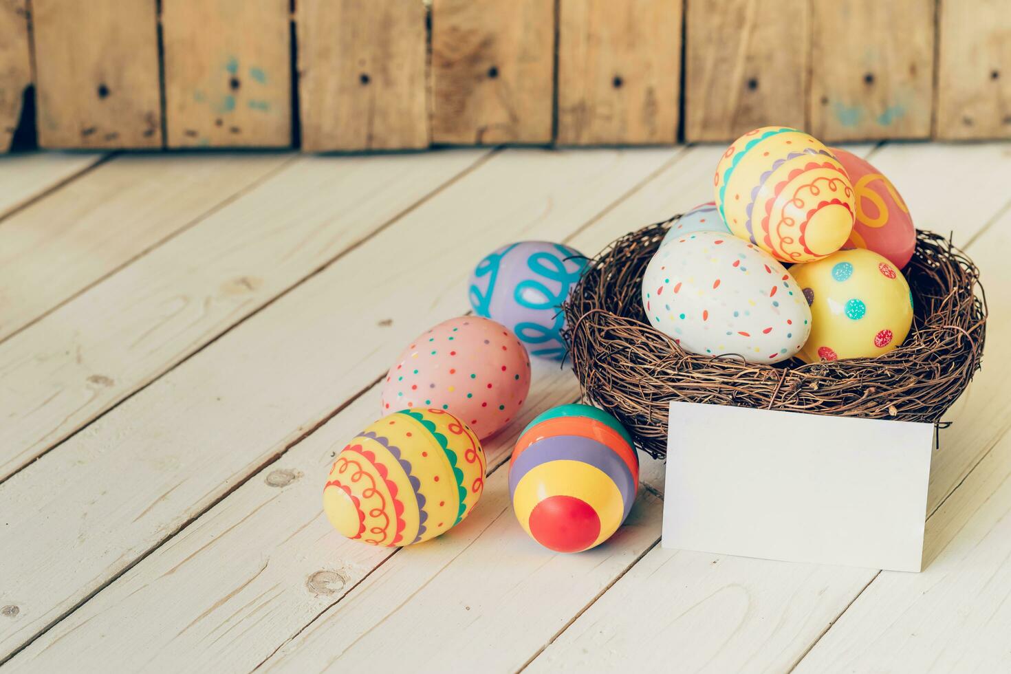 Colorful easter eggs in the nest and paper card on wood table background. photo
