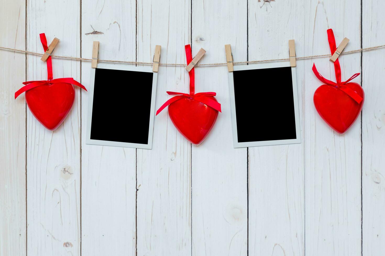 Photo frame blank and red heart hanging on white wood background with space