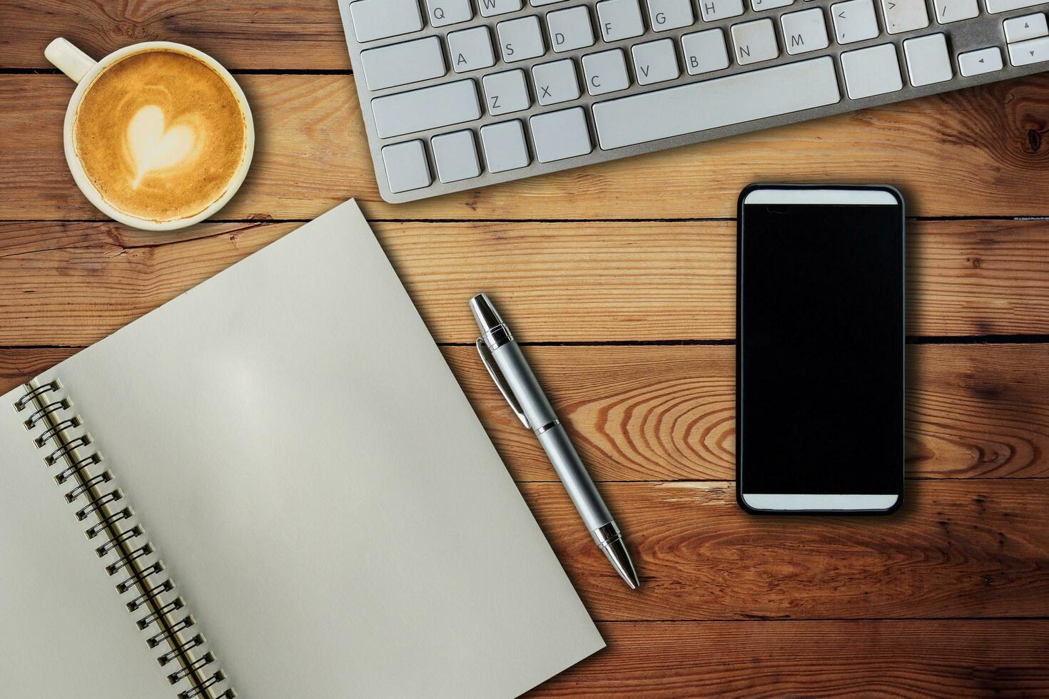 Mobile phone, notebook pen, keyboard computer and coffee cup on office wooden table with copy space. photo