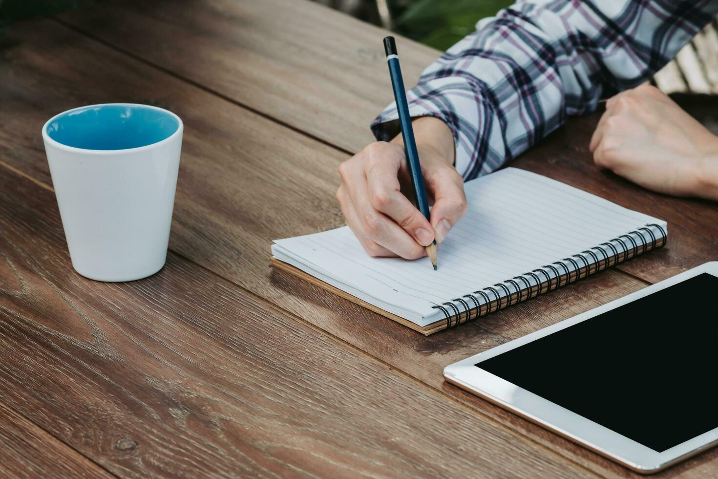 woman hand writing notepad and holding phone on wooden table at coffee shop photo
