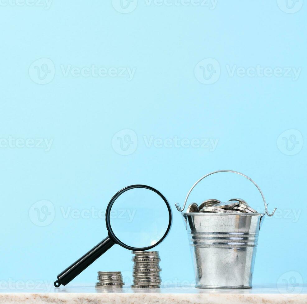 A stack of metal coins and a plastic magnifier on a blue background. The concept of increasing taxes, subsidies photo
