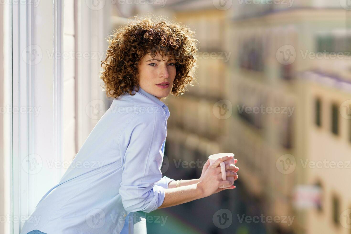 Rizado peludo mujer Bebiendo café en balcón foto