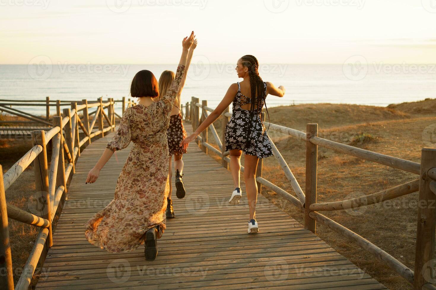Relaxed diverse women joyfully running on boardwalk on seashore photo