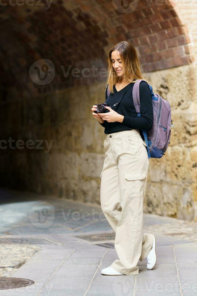 Happy woman photographing aged buildings on street during sightseeing trip photo