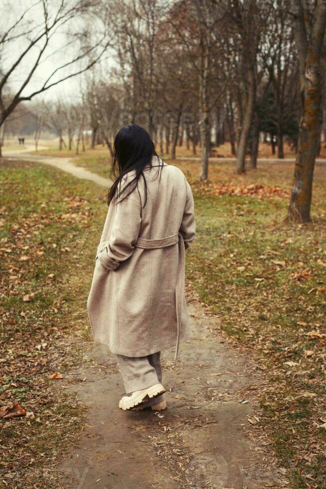 portrait of brunette hair woman in beige coat walking at the city park . photo