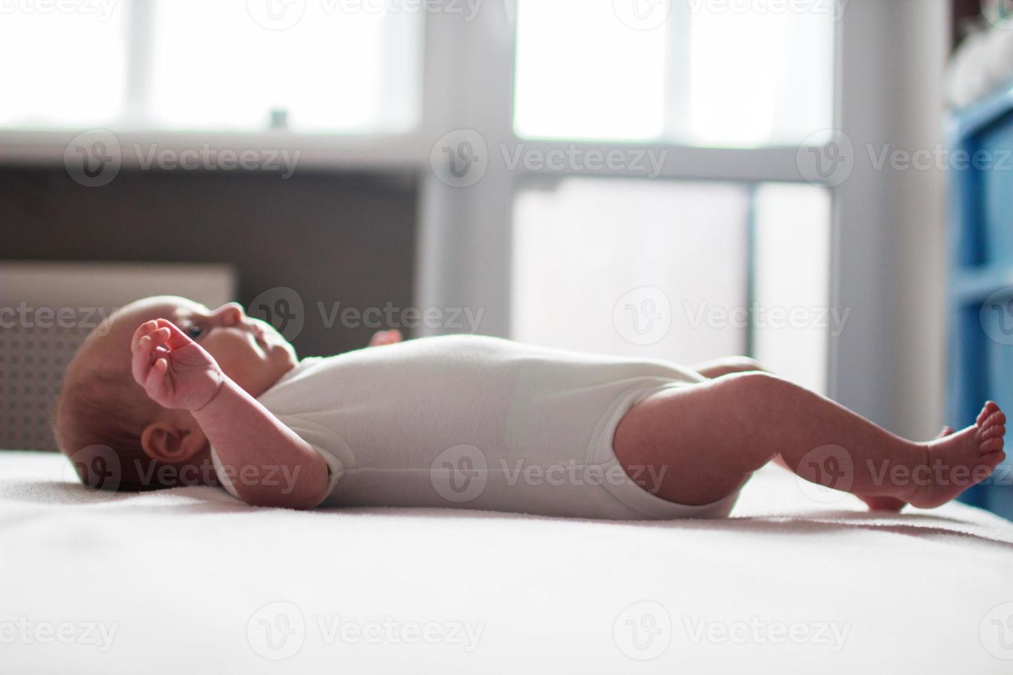 the infant lies on the bed in front of the window photo