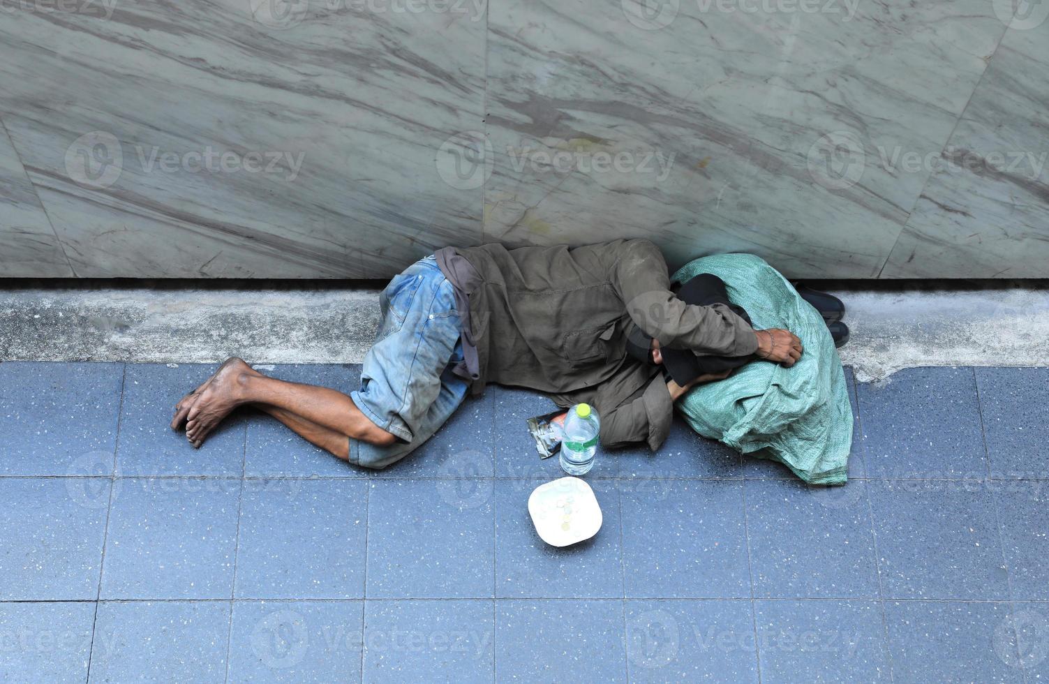 Homeless man sleeping on footpath seeking help from people walking pass. photo