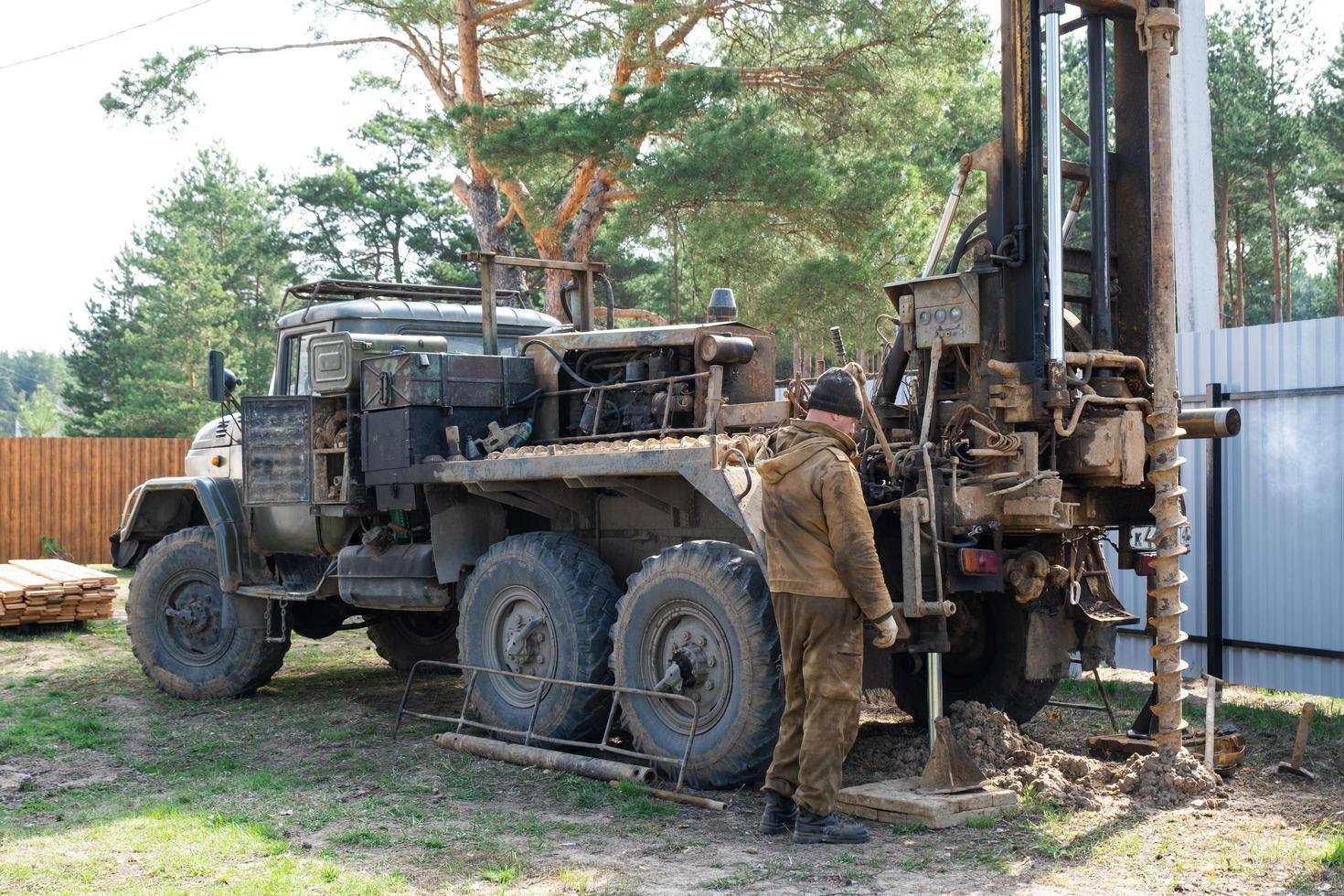 Team of workers with drilling rig on car are drilling artesian well for water in ground. Insertion of metal casing pipe into ground, installation of individual drinking supply, June 28, 2022, Russia, photo