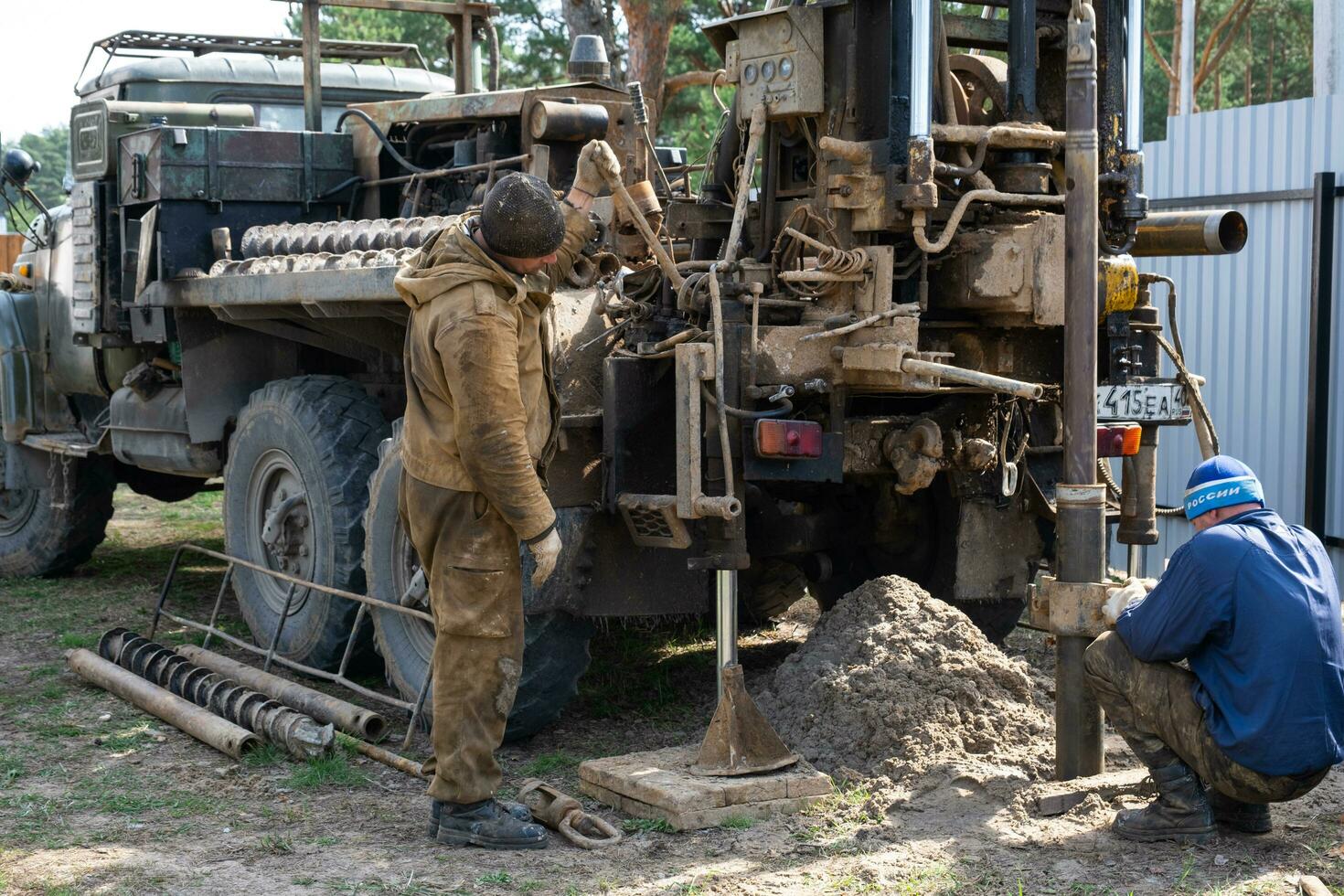 Team of workers with drilling rig on car are drilling artesian well for water in ground. Insertion of metal casing pipe into ground, installation of individual drinking supply, June 28, 2022, Russia, photo