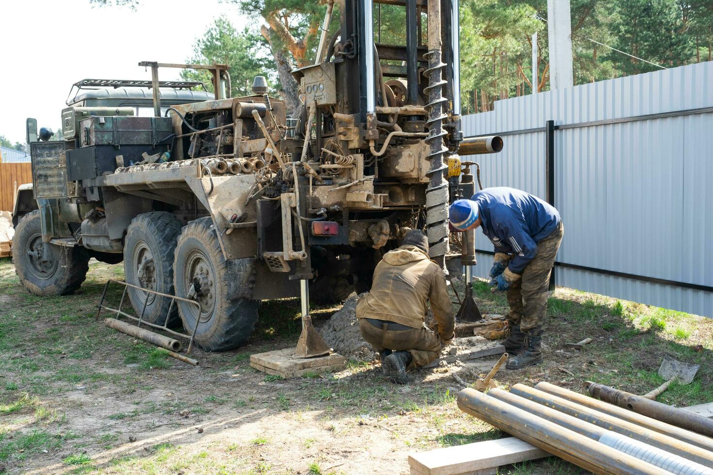 Team of workers with drilling rig on car are drilling artesian well for water in ground. Insertion of metal casing pipe into ground, installation of individual drinking supply, June 28, 2022, Russia, photo