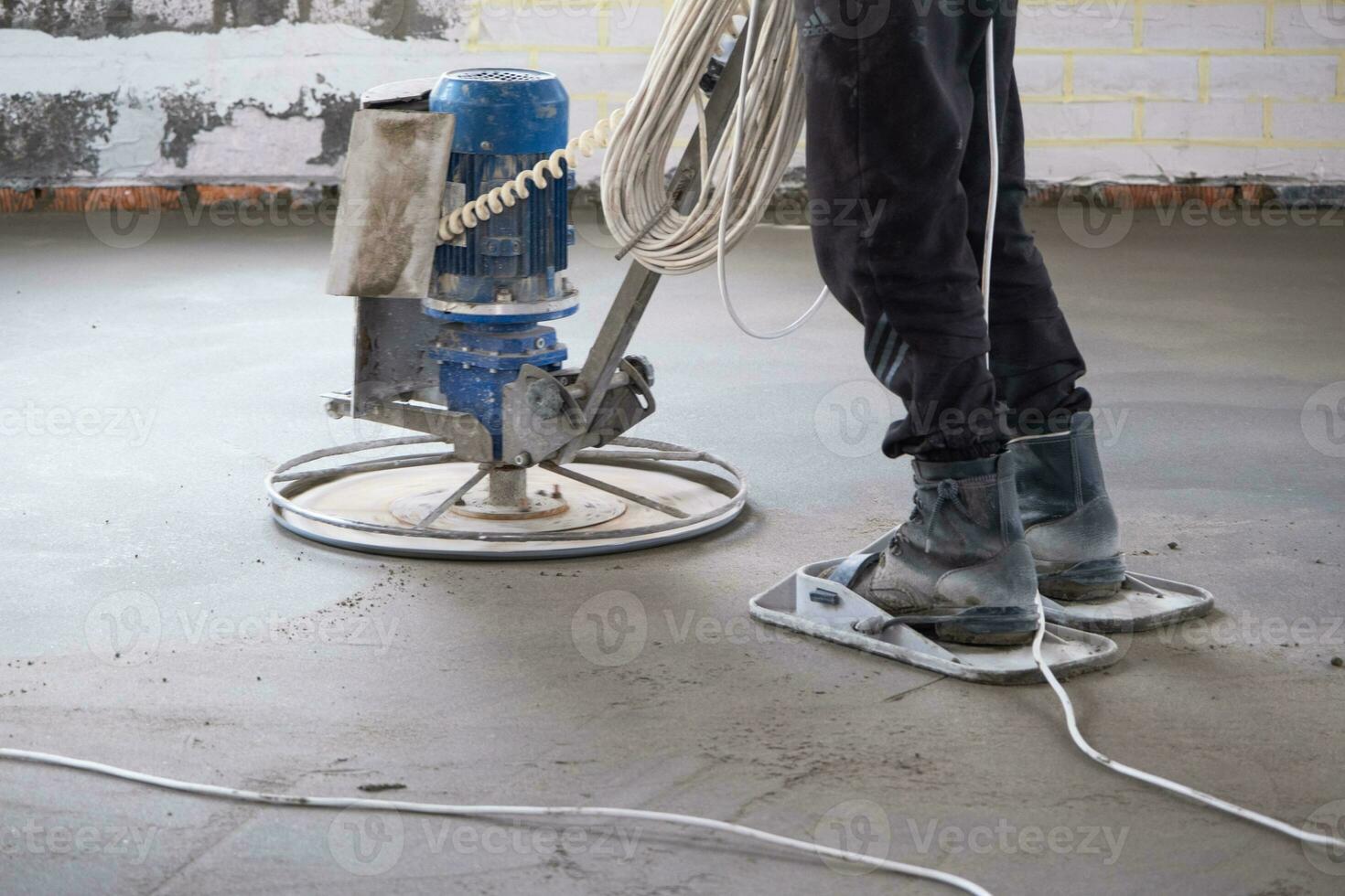 Ramming and grinding of semi-dry floor screed by a machine with a rotating disk for leveling. Construction of a concrete floor in the house, a master with special equipment. photo