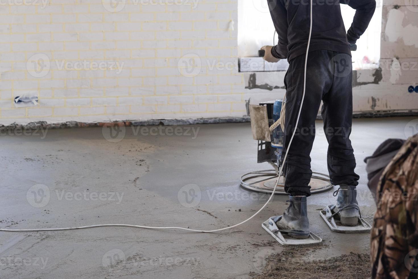 Ramming and grinding of semi-dry floor screed by a machine with a rotating disk for leveling. Construction of a concrete floor in the house, a master with special equipment. photo