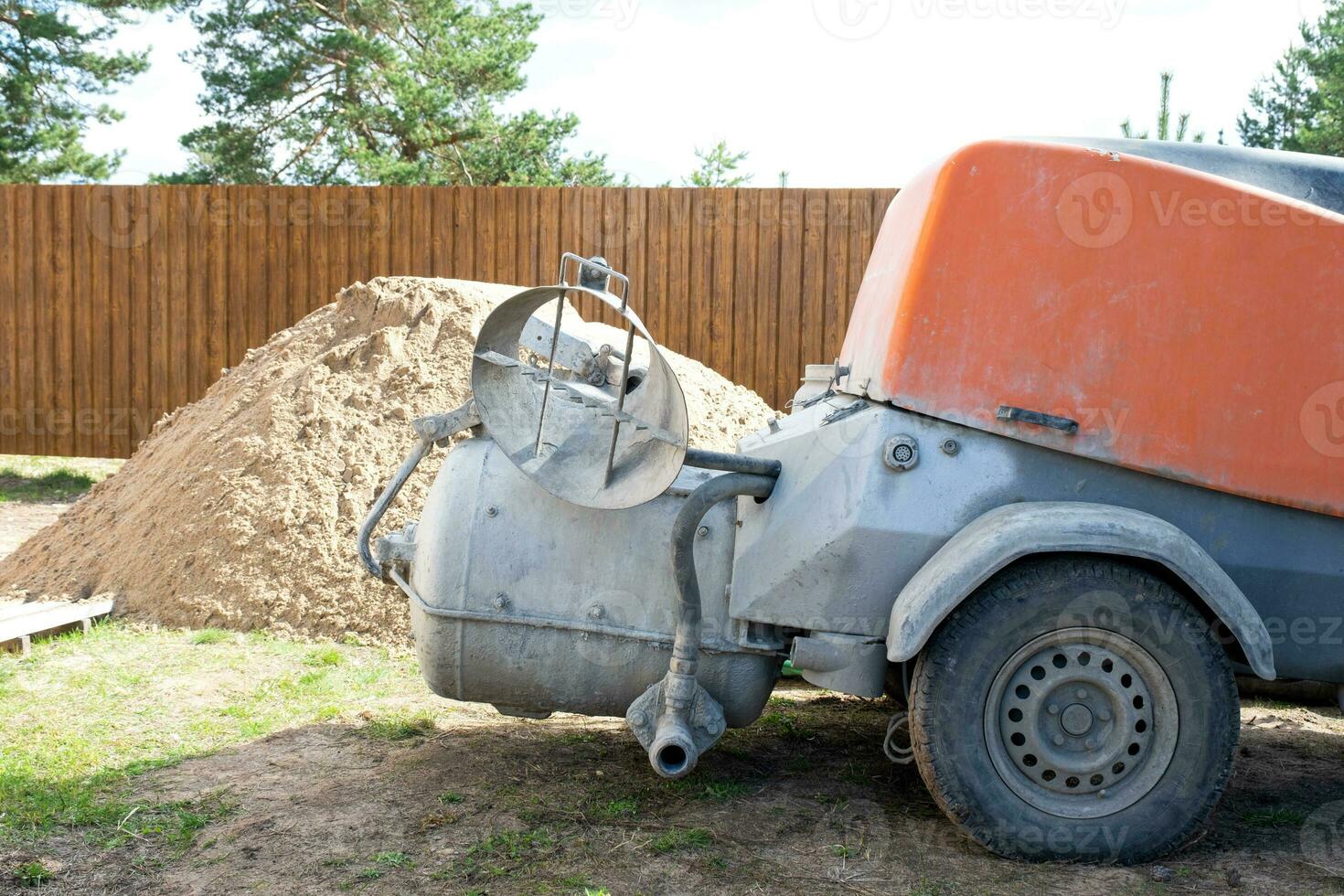 Machine with mixer isinstallation for feeding cement mixture for pouring semi-dry floor screed in house. Construction site with slide of sand, preparation for leveling the rough floor of cottage photo