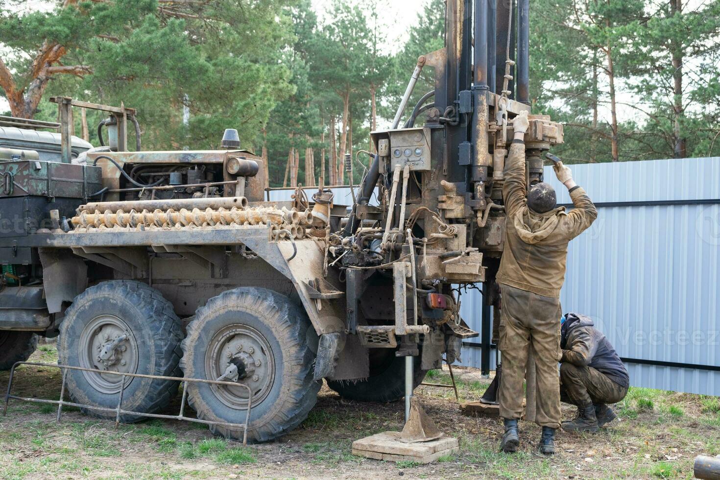 Team of workers with drilling rig on car are drilling artesian well for water in ground. Insertion of metal casing pipe into ground, installation of individual drinking supply, June 28, 2022, Russia, photo