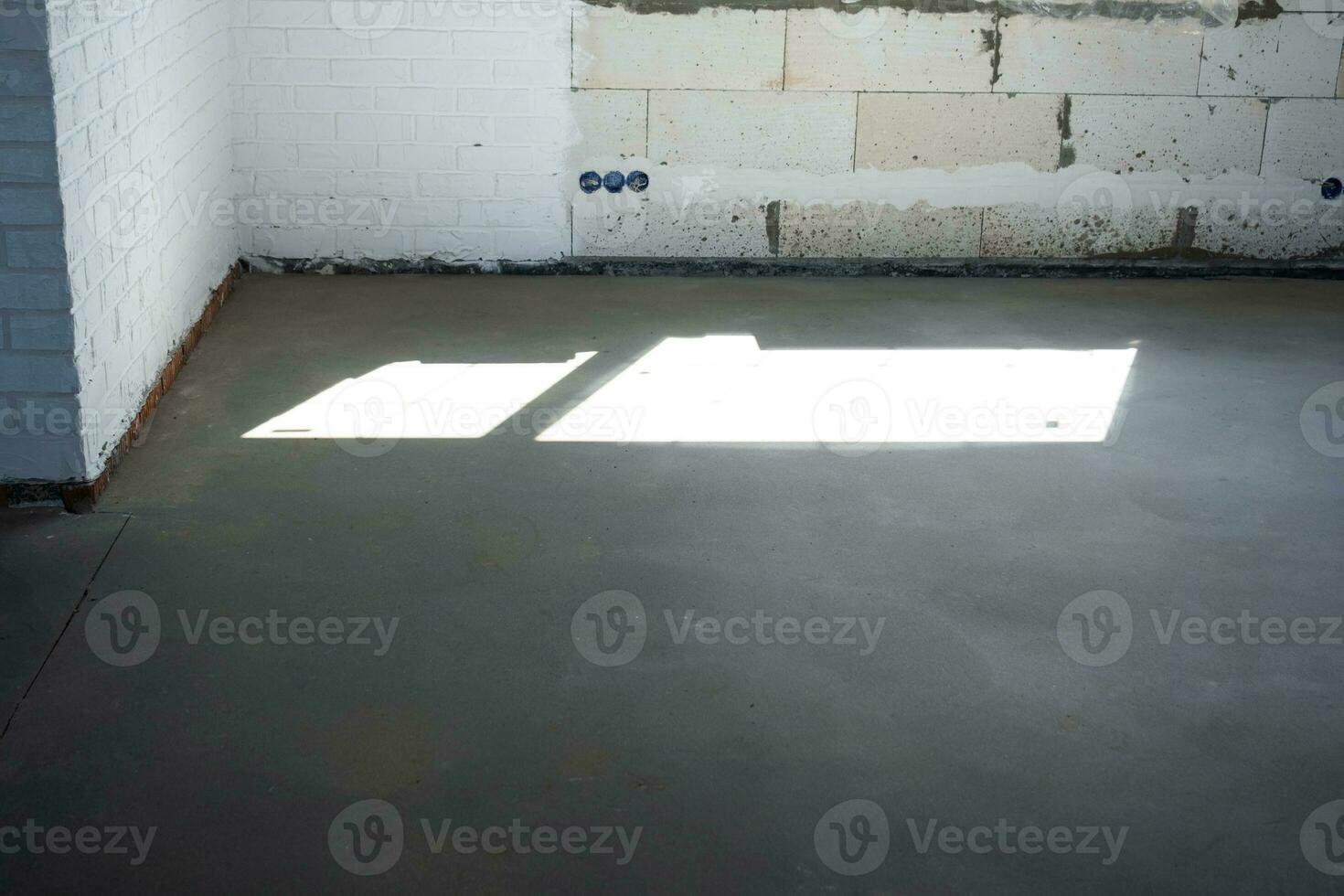 The leveled rough floor in a house under construction with a semi-dry cement screed is a smooth surface with light from the windows photo