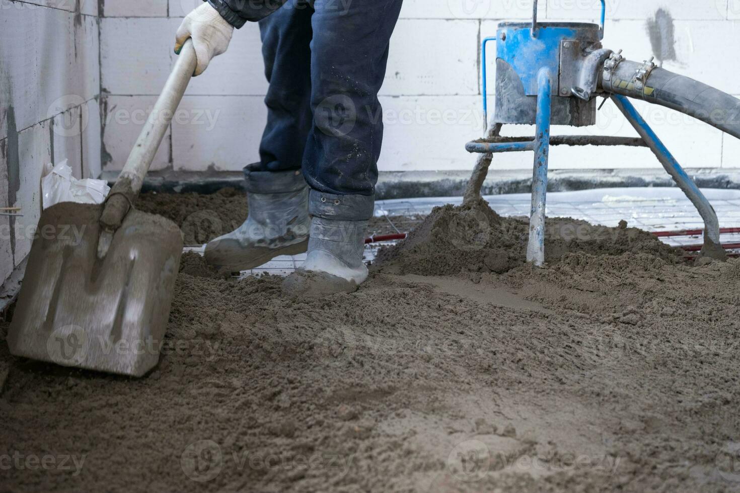 Semi-dry floor screed - a worker shovels a construction mixture through a special sleeve for cementing and leveling on underfloor heating pipes. photo