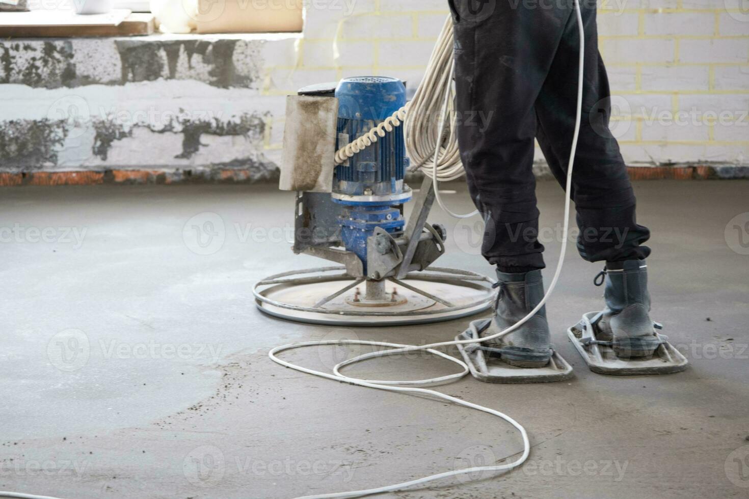 Ramming and grinding of semi-dry floor screed by a machine with a rotating disk for leveling. Construction of a concrete floor in the house, a master with special equipment. photo