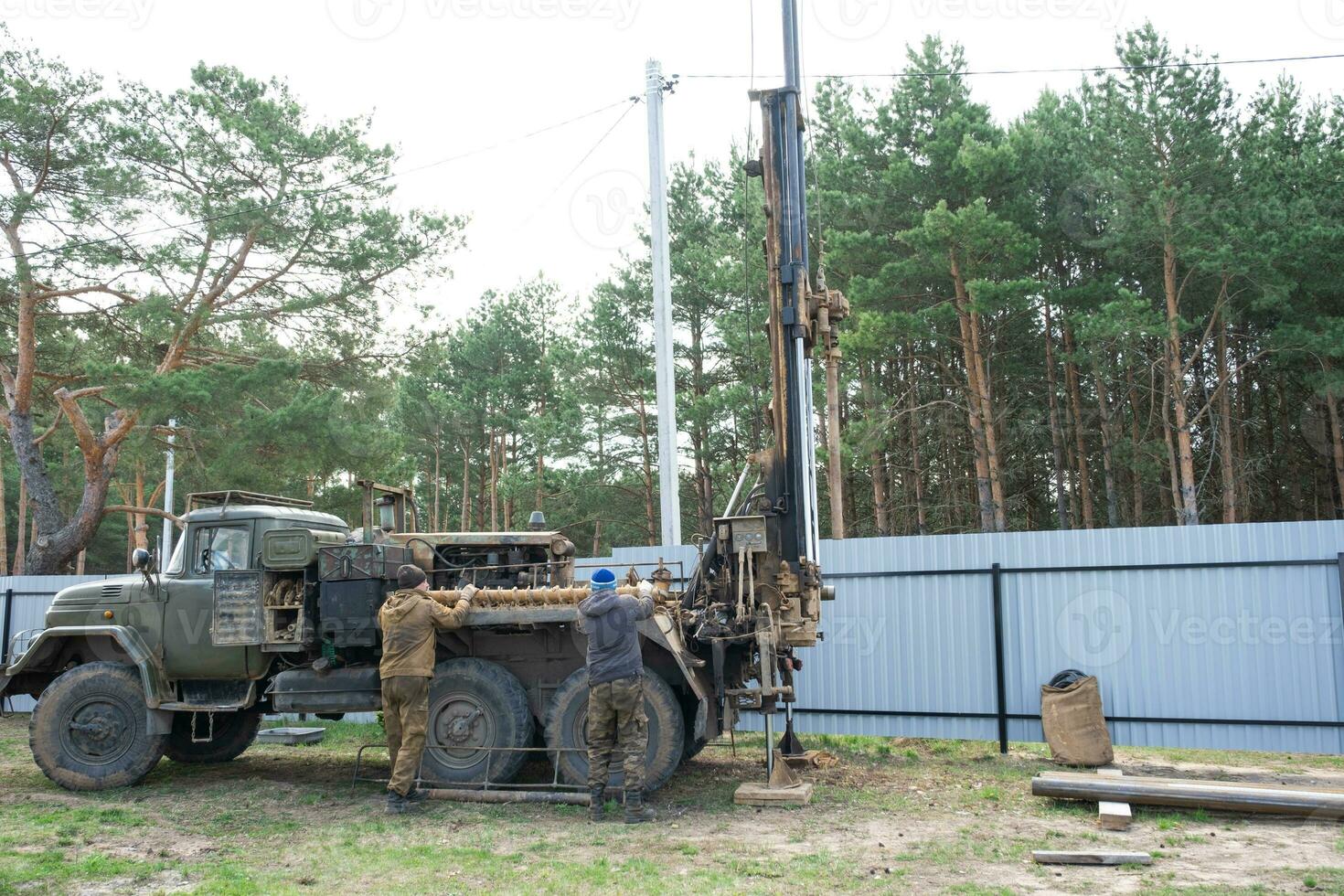 Team of workers with drilling rig on car are drilling artesian well for water in ground. Insertion of metal casing pipe into ground, installation of individual drinking supply, June 28, 2022, Russia, photo