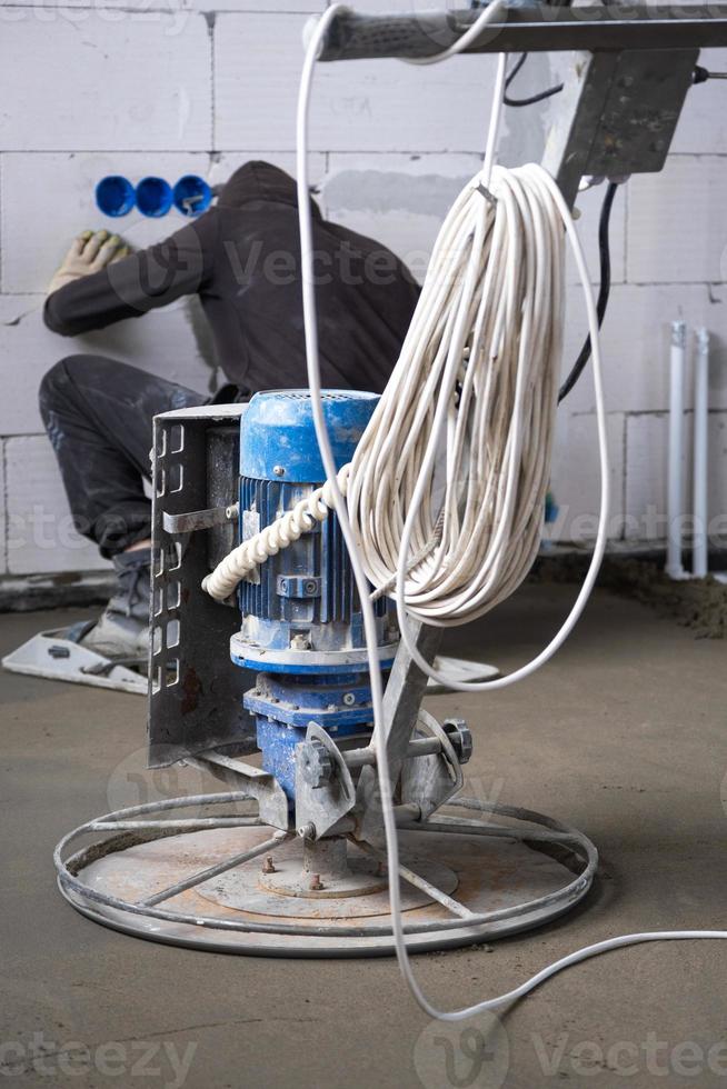 Ramming and grinding of semi-dry floor screed by a machine with a rotating disk for leveling. Construction of a concrete floor in the house, a master with special equipment. photo