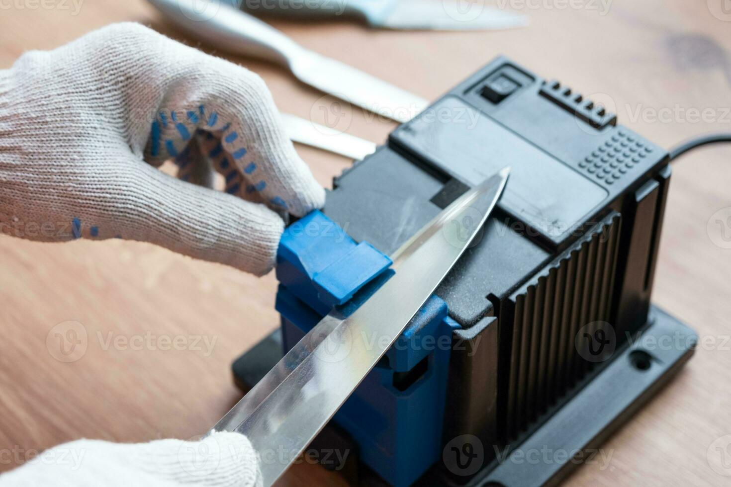 Sharpening a knife on an electric sharpener at home. The man's hand drives the knife blade between the blue sharpeners, dust flies on the machine. photo