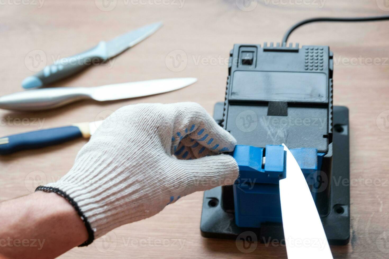 Sharpening a knife on an electric sharpener at home. The man's hand drives the knife blade between the blue sharpeners, dust flies on the machine. photo