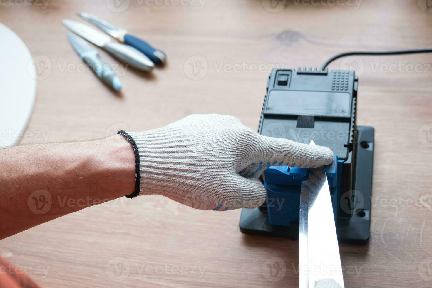 Sharpening a knife on an electric sharpener at home. The man's hand drives the knife blade between the blue sharpeners, dust flies on the machine. photo