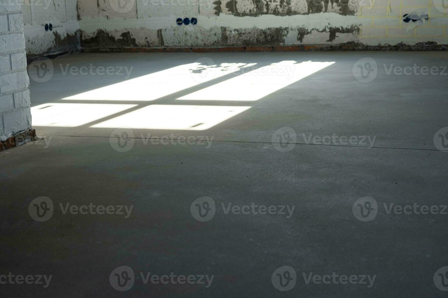 The leveled rough floor in a house under construction with a semi-dry cement screed is a smooth surface with light from the windows photo