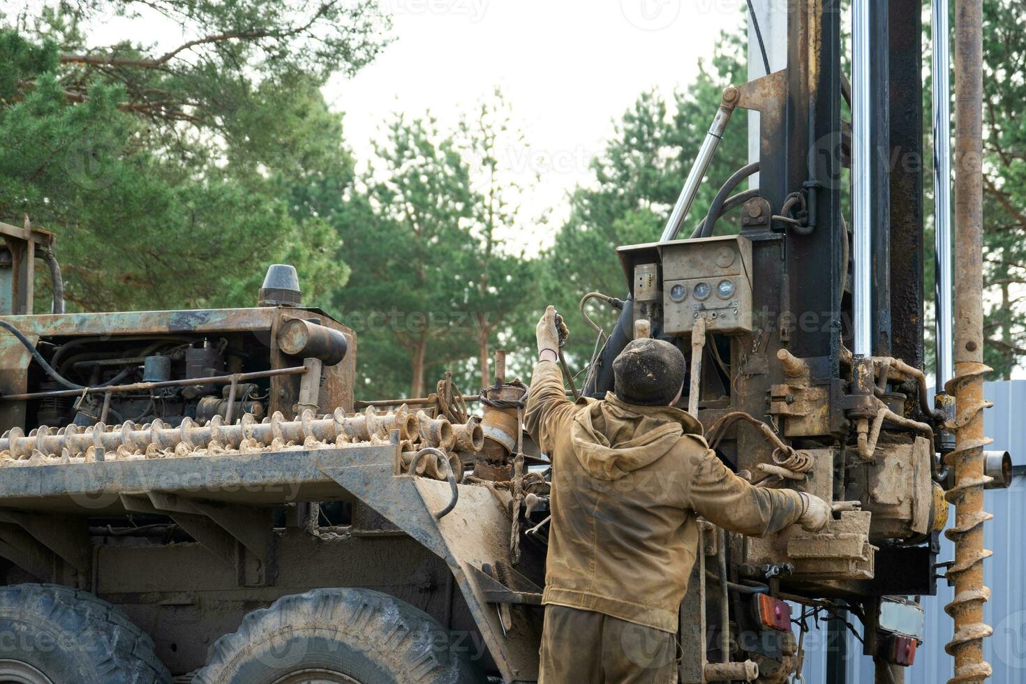 Team of workers with drilling rig on car are drilling artesian well for water in ground. Insertion of metal casing pipe into ground, installation of individual drinking supply, June 28, 2022, Russia, photo