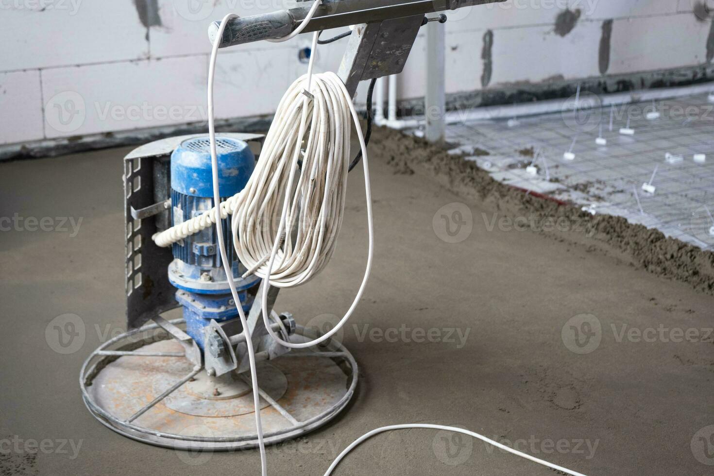 Ramming and grinding of semi-dry floor screed by a machine with a rotating disk for leveling. Construction of a concrete floor in the house, a master with special equipment. photo