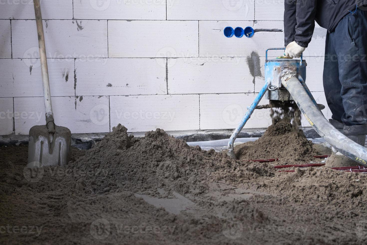 Semi-dry floor screed - a worker shovels a construction mixture through a special sleeve for cementing and leveling on underfloor heating pipes. photo