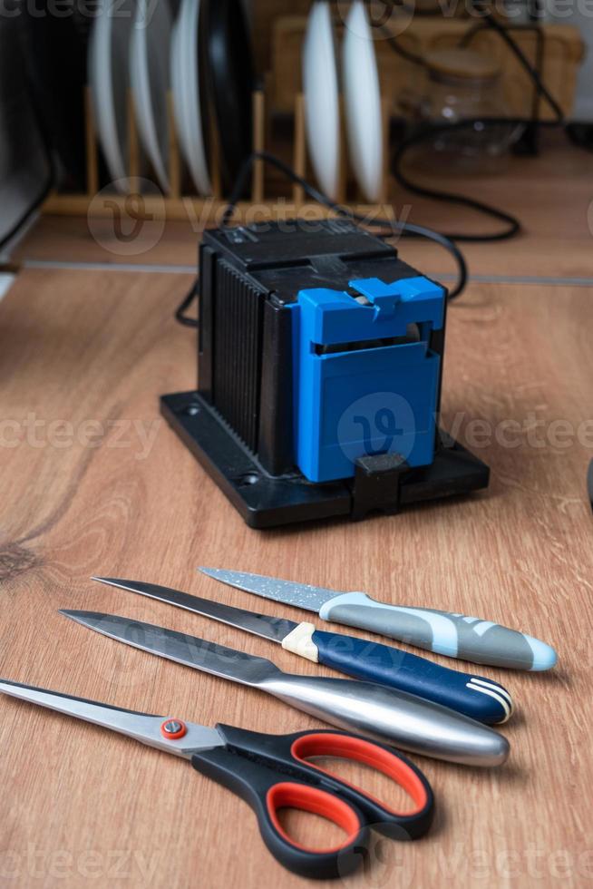 Sharpening a knife on an electric sharpener at home. Flatlay knife blade, scissors, sharpeners, dust flies on the machine. photo