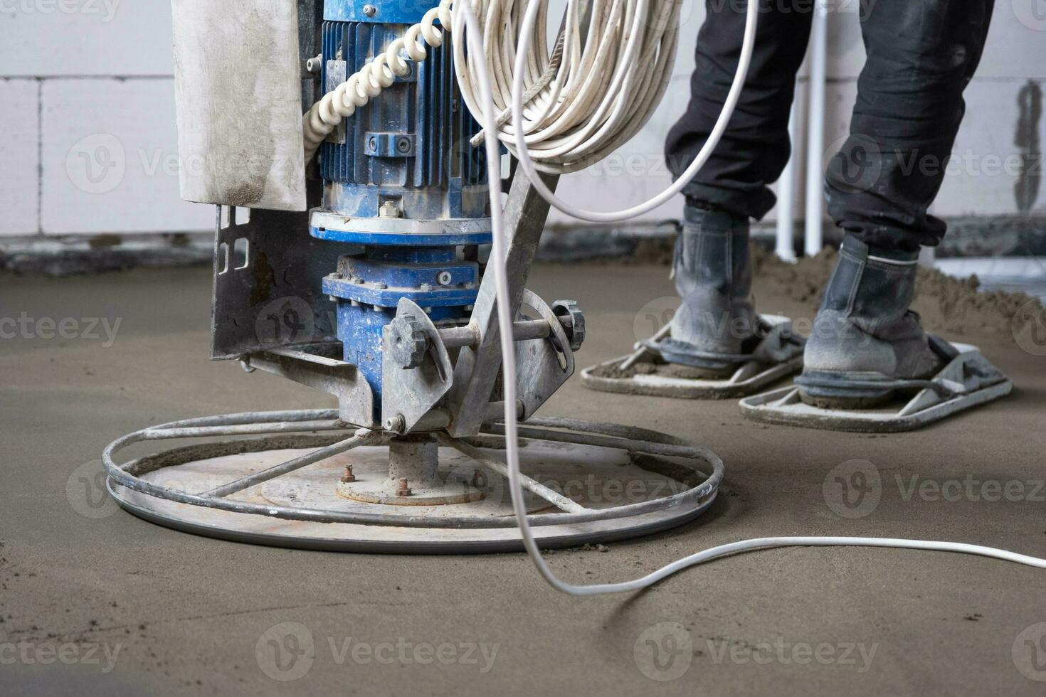 Ramming and grinding of semi-dry floor screed by a machine with a rotating disk for leveling. Construction of a concrete floor in the house, a master with special equipment. photo