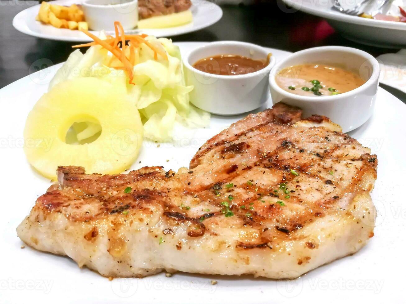 Twin T-bone pork steak with fruit salad,  pepper and tomato sauce on white ceramic plate on black leather table in the restaurant. photo