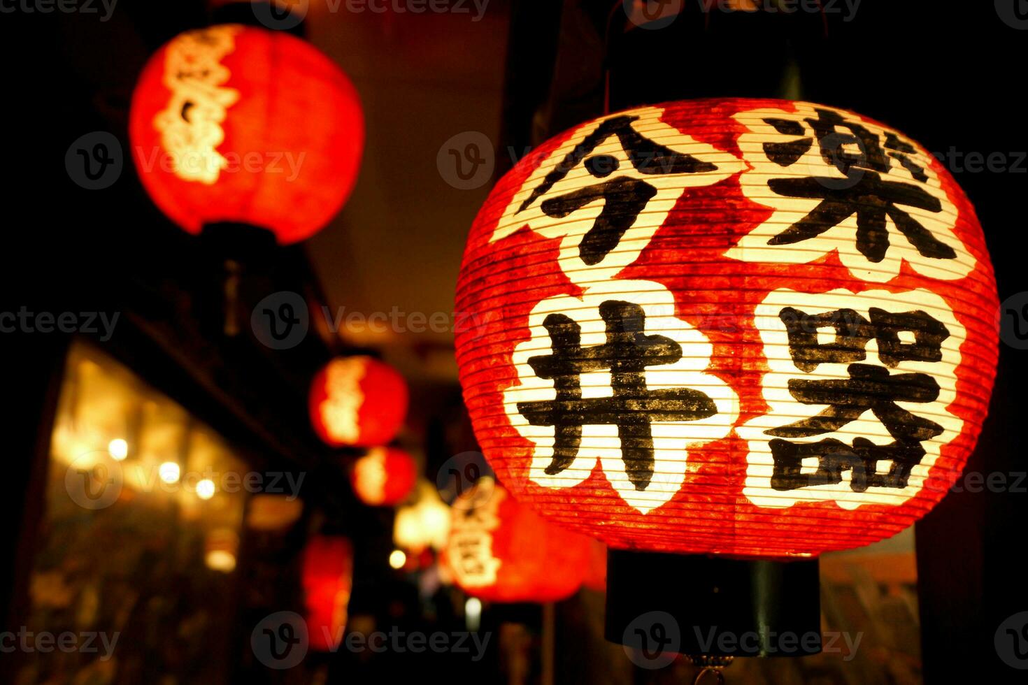 Black Japanese texts on red paper lantern hanging under Japanese restaurant eaves on night time with blurry background. photo