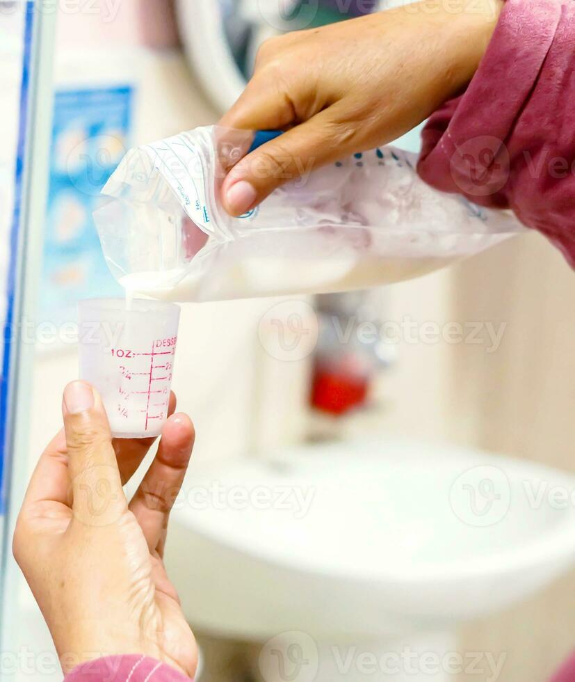 The nurse's hands is pouring mother's fresh milk from the plastic bag for milk storage to medicine measuring glass cup for sick newborn baby in the hospital. photo