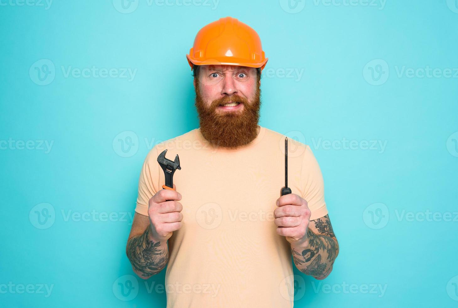 Confused man with screwdriver and spanners. worried and uncertain expression. cyan background photo